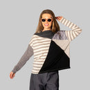 Person wearing a geometric patterned sweater and dark pants against a plain wall.