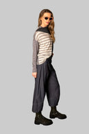 Person wearing a striped sweater and dark pants against a plain wall.