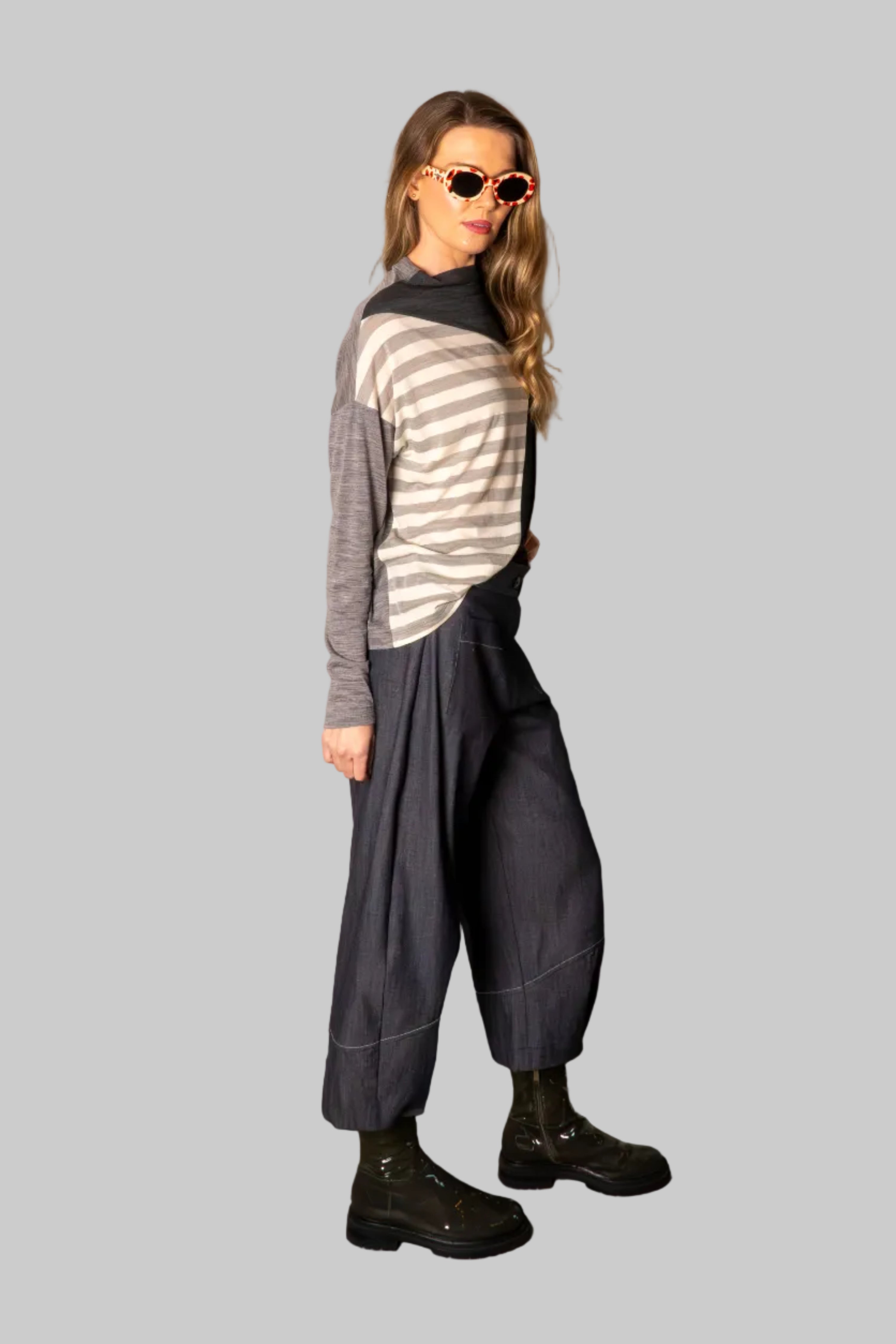 Person wearing a striped sweater and dark pants against a plain wall.