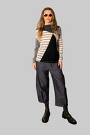 Person wearing a striped sweater and gray pants against a plain wall.
