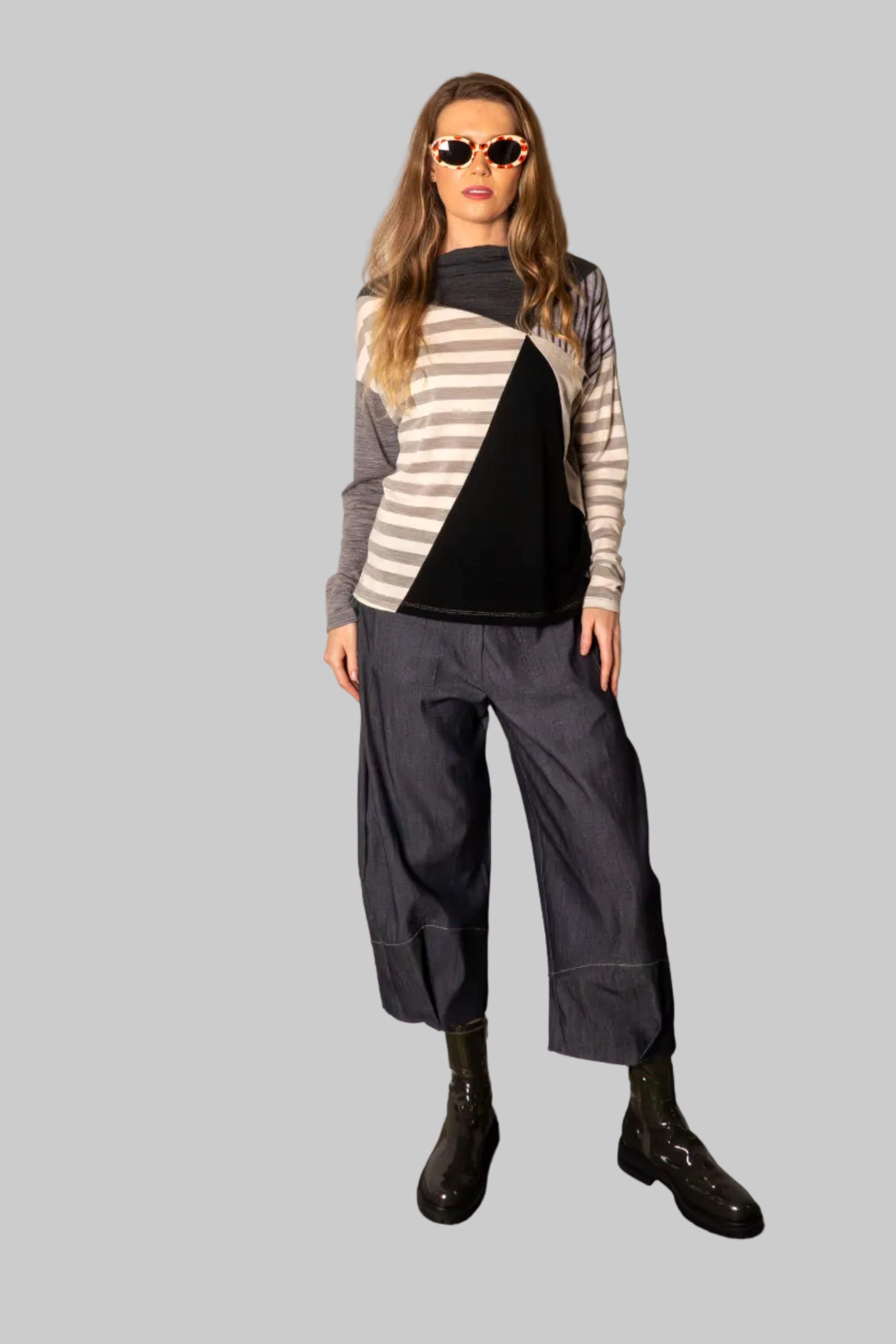 Person wearing a striped sweater and gray pants against a plain wall.
