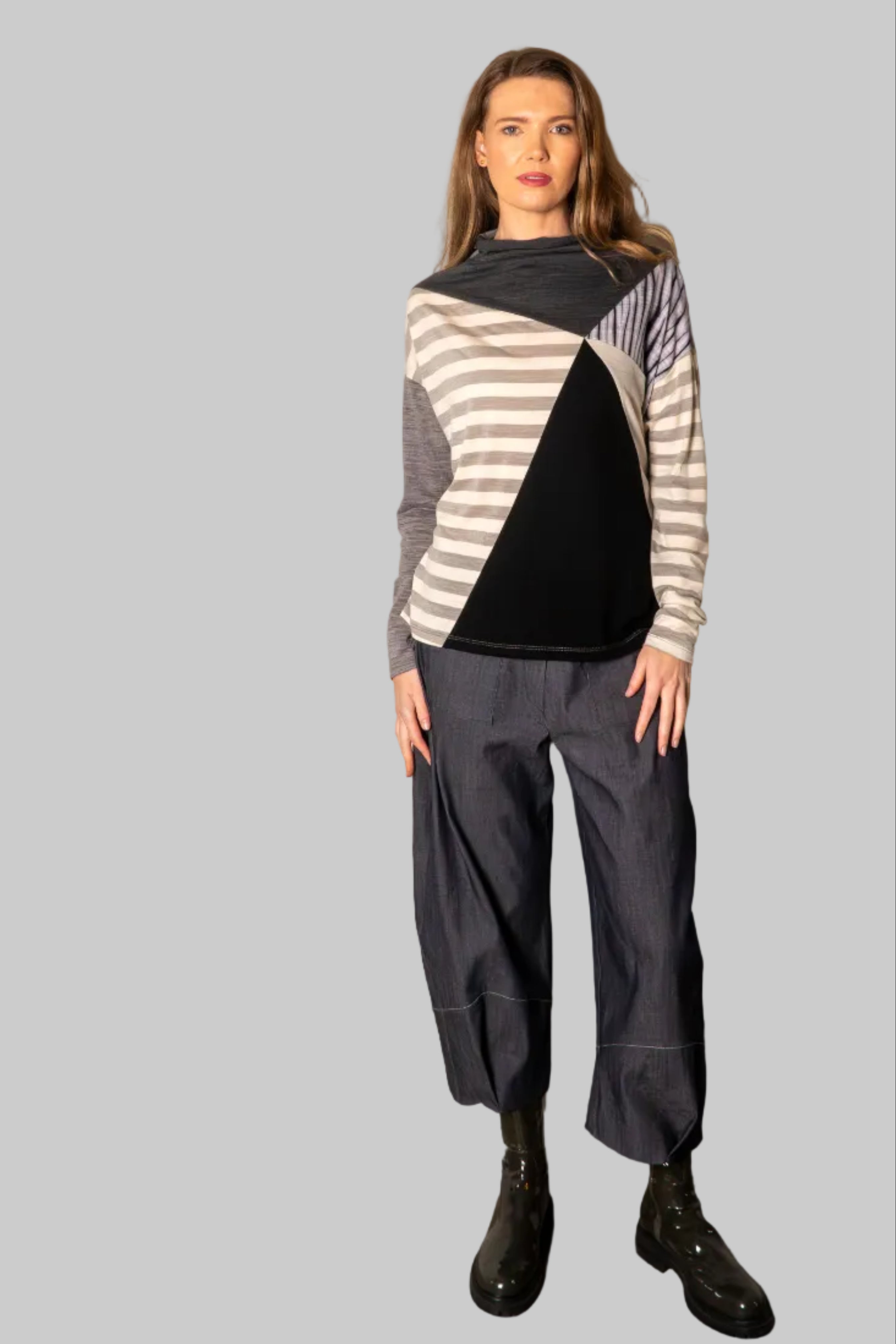 Person wearing a striped sweater and gray pants against a plain wall.