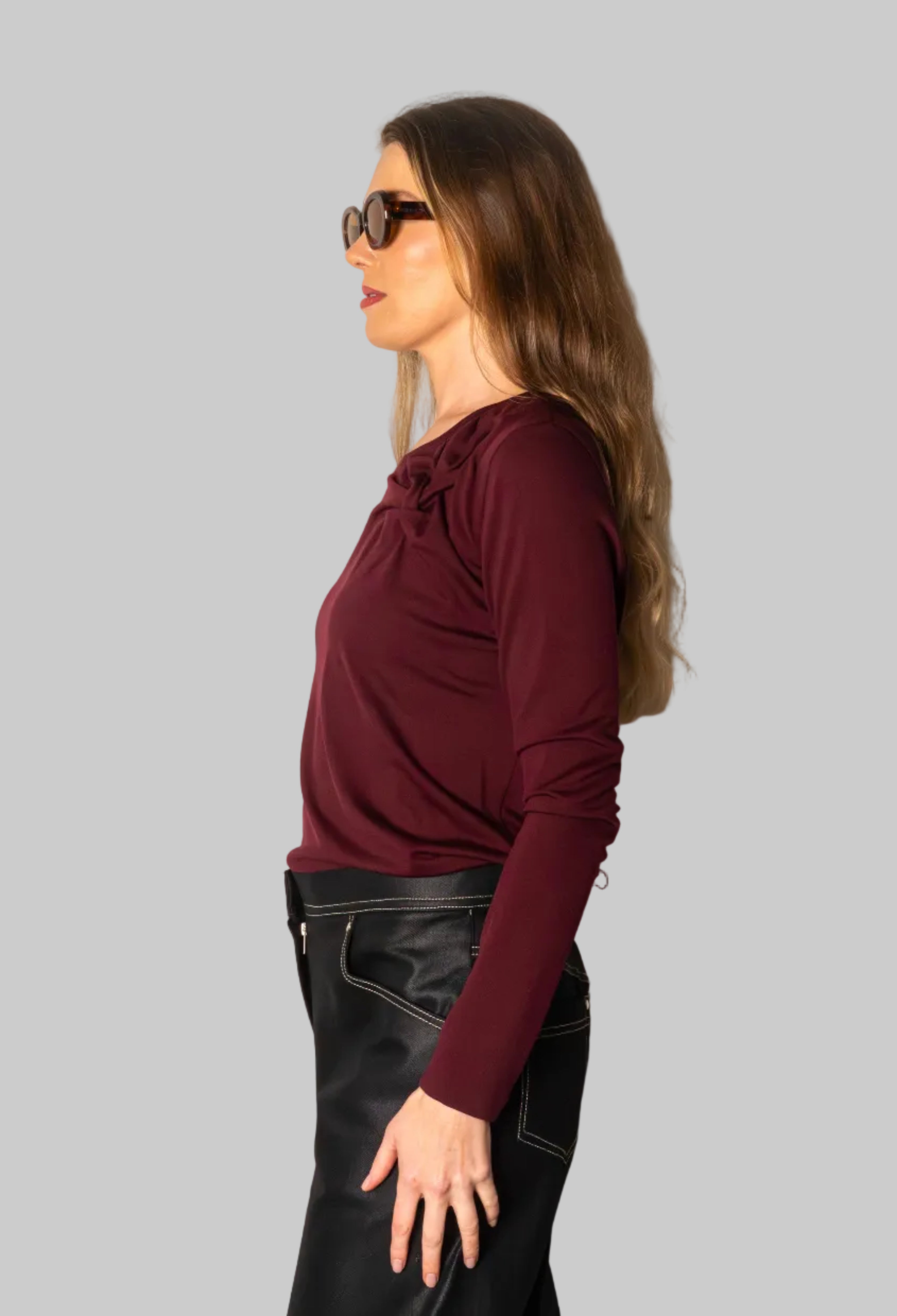 Woman wearing a burgundy top and black pants against a white wall